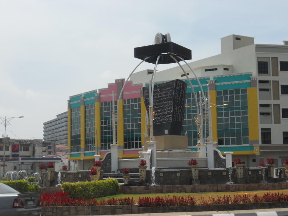 Batu Bersurat Terengganu, gambar pameran muzium. Tahunnya tidak dapat dibaca — baris yang terukir dengan tarikh mengalami kerosakan fizikal. Para sarjana filologi memberikan tiga tafsiran berbeza, iaitu 1303, 1308, atau 1387, tanpa ada kata putus, malah tiada sebarang pentarikhan fizikal-kimia telah dibuat setakat ini. Batu ini menjadi bukti kepada satu perkara: walau ada batu bersurat di hadapan kita, ia belum tentu dapat memberitahu bilakah tahun ia didirikan.